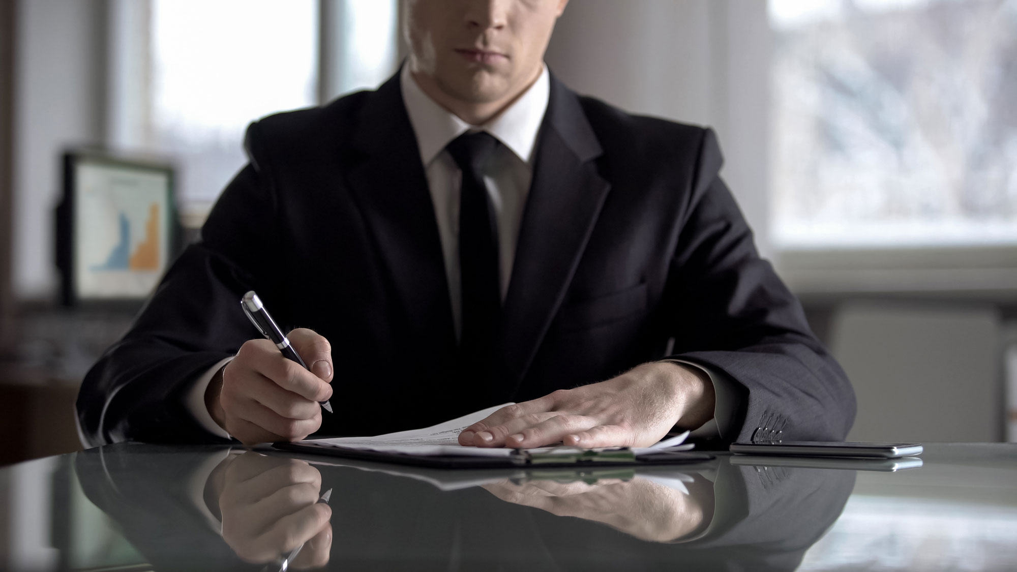 A business man sitting at a table about to sign a form